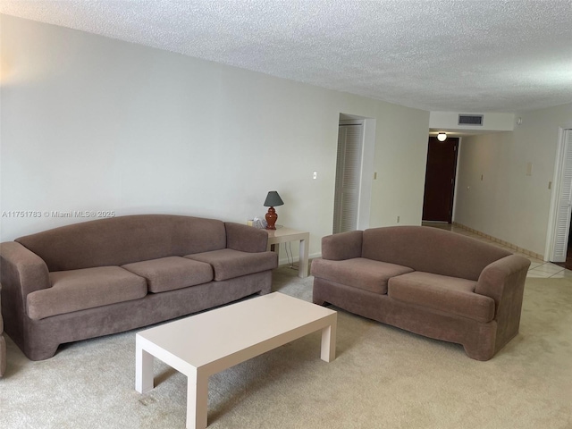 living room with a textured ceiling, baseboards, visible vents, and light colored carpet