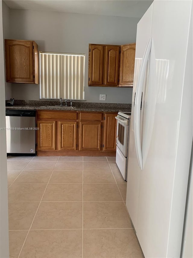 kitchen featuring light tile patterned floors, white appliances, a sink, brown cabinetry, and dark countertops