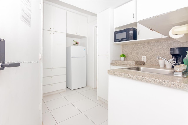 kitchen featuring black microwave, a sink, white cabinetry, light countertops, and freestanding refrigerator