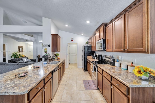 kitchen with brown cabinetry, lofted ceiling, open floor plan, stainless steel appliances, and a sink