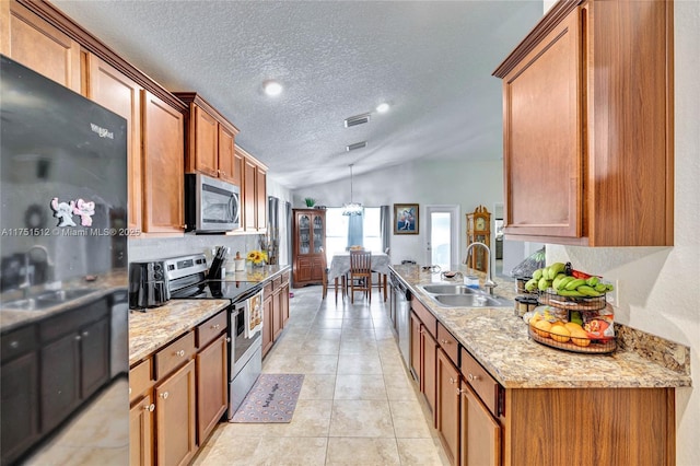 kitchen featuring visible vents, lofted ceiling, appliances with stainless steel finishes, brown cabinets, and a sink