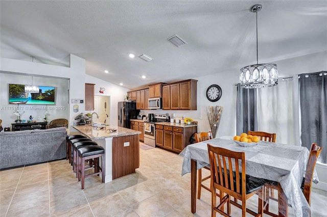 kitchen featuring visible vents, light stone counters, a peninsula, stainless steel appliances, and pendant lighting