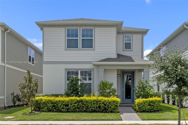 traditional home with stucco siding, roof with shingles, and a front yard