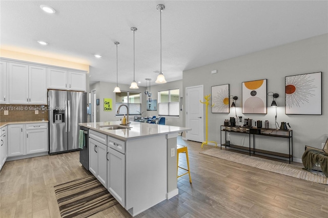 kitchen with an island with sink, stainless steel appliances, light countertops, white cabinetry, and a sink