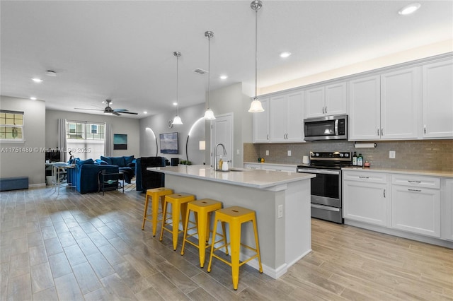 kitchen featuring white cabinets, a kitchen island with sink, appliances with stainless steel finishes, and light countertops