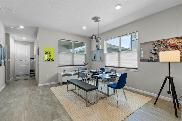 dining area featuring a textured ceiling, light wood-type flooring, and baseboards