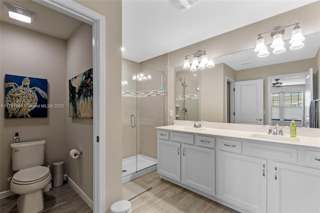 full bath featuring toilet, wood finished floors, a sink, double vanity, and a stall shower