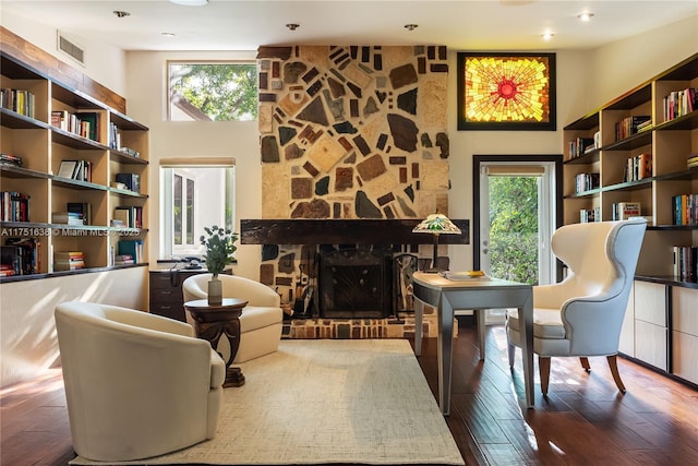 sitting room with a healthy amount of sunlight, a fireplace, a towering ceiling, and wood finished floors