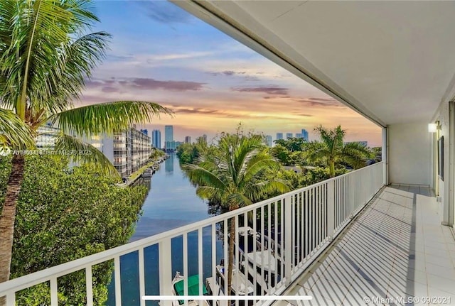 balcony at dusk featuring a view of city and a water view