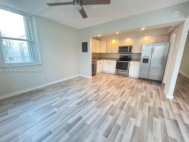 kitchen featuring appliances with stainless steel finishes, light wood-style floors, a ceiling fan, white cabinetry, and baseboards