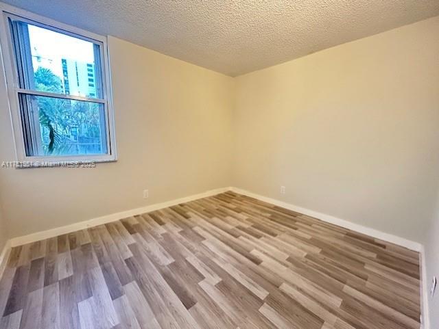 spare room with a textured ceiling, wood finished floors, and baseboards