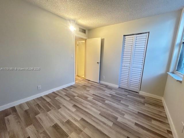 unfurnished bedroom with light wood finished floors, a closet, baseboards, and a textured ceiling