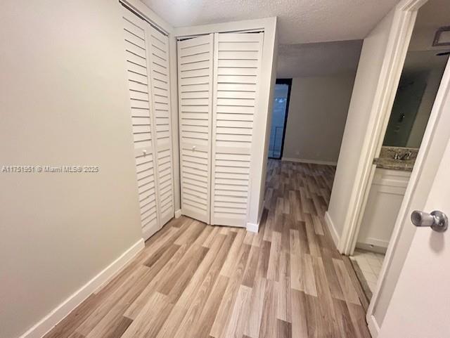 hallway with light wood finished floors, baseboards, and a textured ceiling