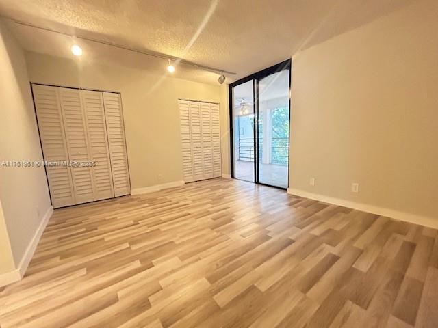 unfurnished room featuring baseboards, a wall of windows, rail lighting, and light wood-style floors