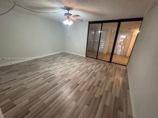 spare room featuring a textured ceiling, wood finished floors, a ceiling fan, and baseboards