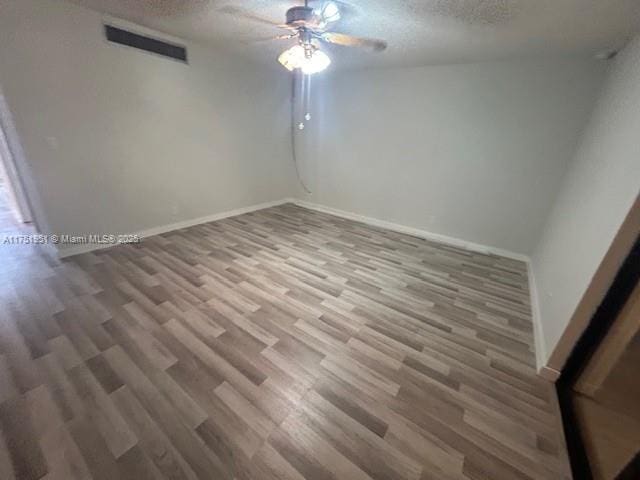 spare room featuring baseboards, visible vents, ceiling fan, wood finished floors, and a textured ceiling