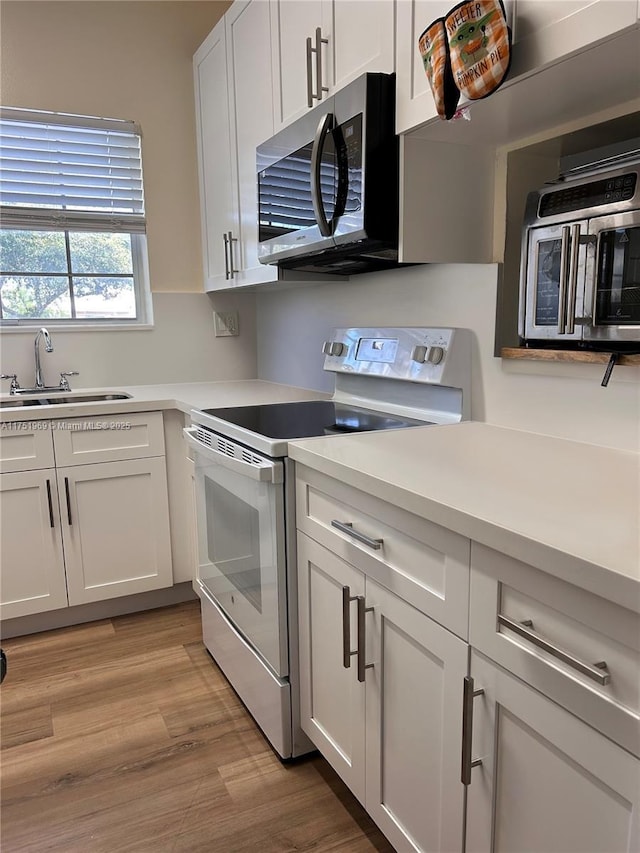 kitchen with a sink, stainless steel microwave, light countertops, and white range with electric cooktop