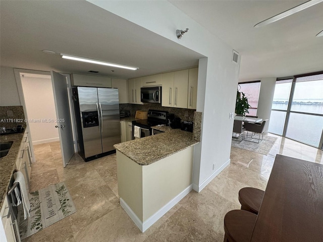 2025 Brickell Ave Unit 901, Miami, FL 33129 - kitchen with stainless steel appliances, backsplash, dark stone counters, a wall of windows, and a peninsula