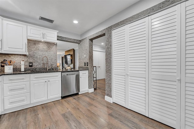 kitchen with light wood finished floors, visible vents, dark stone counters, stainless steel dishwasher, and a sink