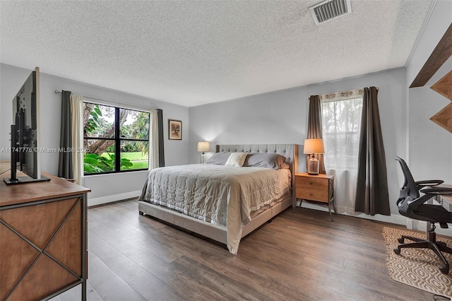 bedroom with a textured ceiling, wood finished floors, visible vents, and baseboards