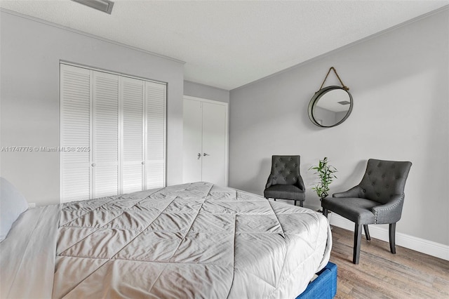 bedroom with a textured ceiling, wood finished floors, visible vents, baseboards, and a closet