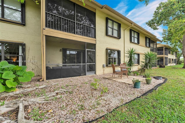 rear view of property featuring a sunroom, a patio, a lawn, and stucco siding
