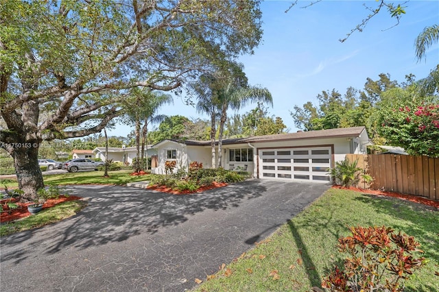 mid-century inspired home featuring aphalt driveway, an attached garage, fence, and a front lawn