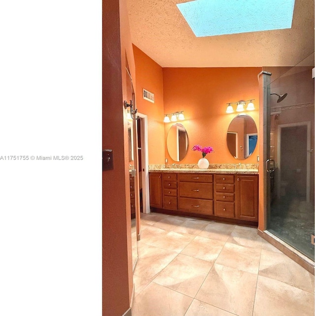 bathroom featuring a textured ceiling, vaulted ceiling with skylight, visible vents, double vanity, and a stall shower