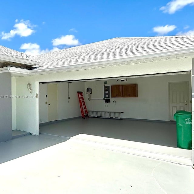 exterior space with a garage, roof with shingles, and stucco siding