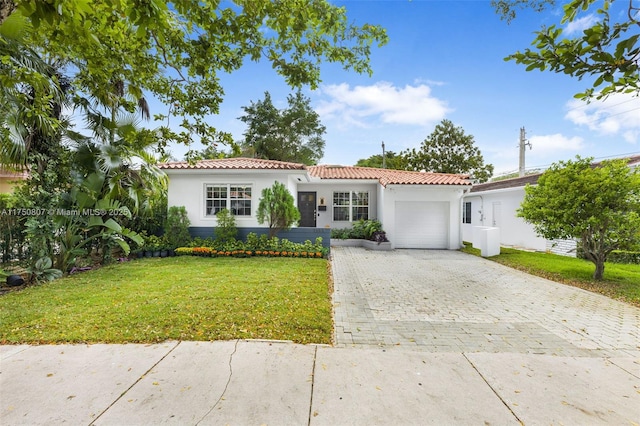 mediterranean / spanish house featuring a garage, a tiled roof, decorative driveway, a front lawn, and stucco siding