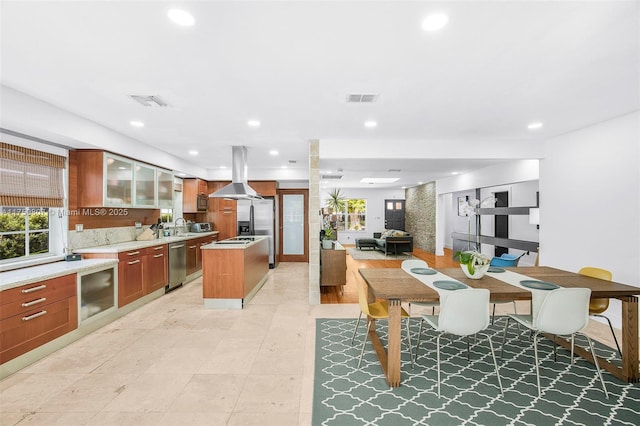 kitchen featuring visible vents, light countertops, dishwasher, island exhaust hood, and glass insert cabinets