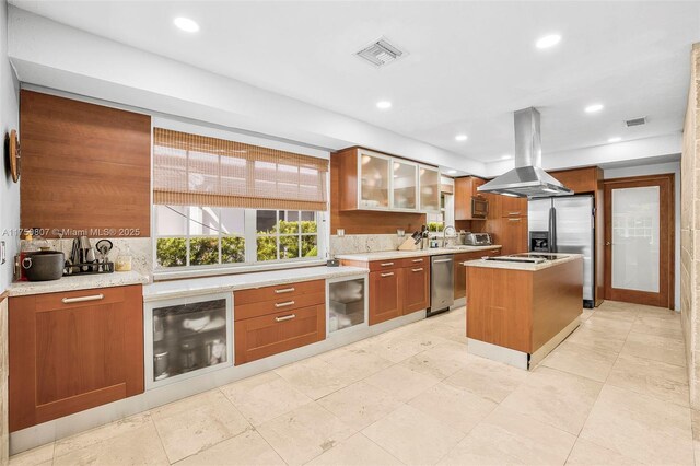 kitchen with visible vents, glass insert cabinets, brown cabinetry, a kitchen island, and island range hood