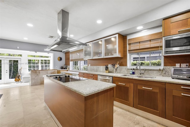 kitchen with glass insert cabinets, brown cabinets, appliances with stainless steel finishes, island exhaust hood, and a sink