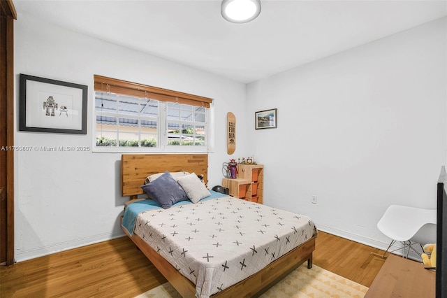 bedroom featuring arched walkways, light wood-style flooring, and baseboards