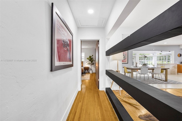corridor featuring attic access, baseboards, and light wood finished floors