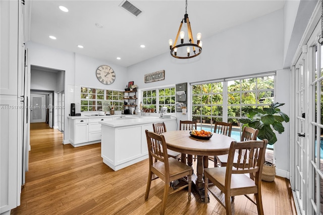 dining room featuring a healthy amount of sunlight, visible vents, light wood-style flooring, and a high ceiling