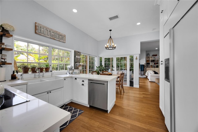 kitchen featuring white cabinets, a peninsula, light countertops, pendant lighting, and stainless steel dishwasher