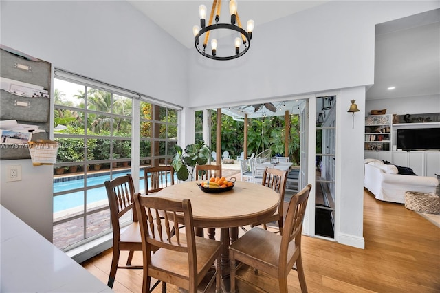 dining area featuring light wood finished floors, a high ceiling, a wealth of natural light, and an inviting chandelier