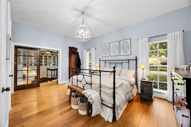 bedroom featuring light wood-type flooring, french doors, baseboards, and an inviting chandelier