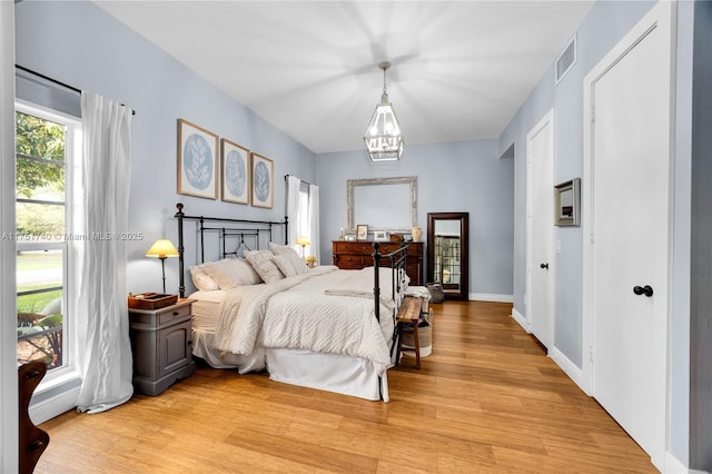 bedroom with an inviting chandelier, light wood-style flooring, visible vents, and baseboards