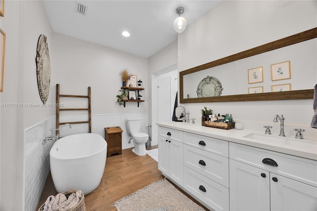 full bath with double vanity, visible vents, wainscoting, a soaking tub, and a sink