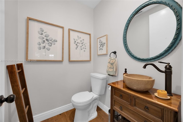 half bath with toilet, baseboards, wood finished floors, and vanity