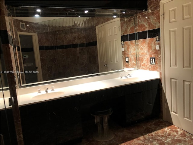 full bathroom with tile walls, marble finish floor, a sink, and double vanity
