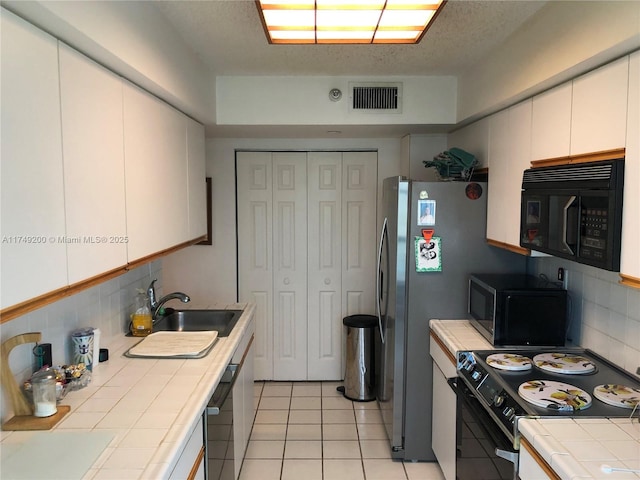 kitchen featuring tile counters, a sink, black appliances, decorative backsplash, and visible vents