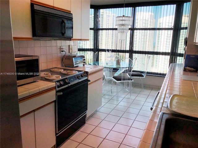 kitchen featuring tile counters, electric stove, black microwave, light tile patterned floors, and stainless steel microwave
