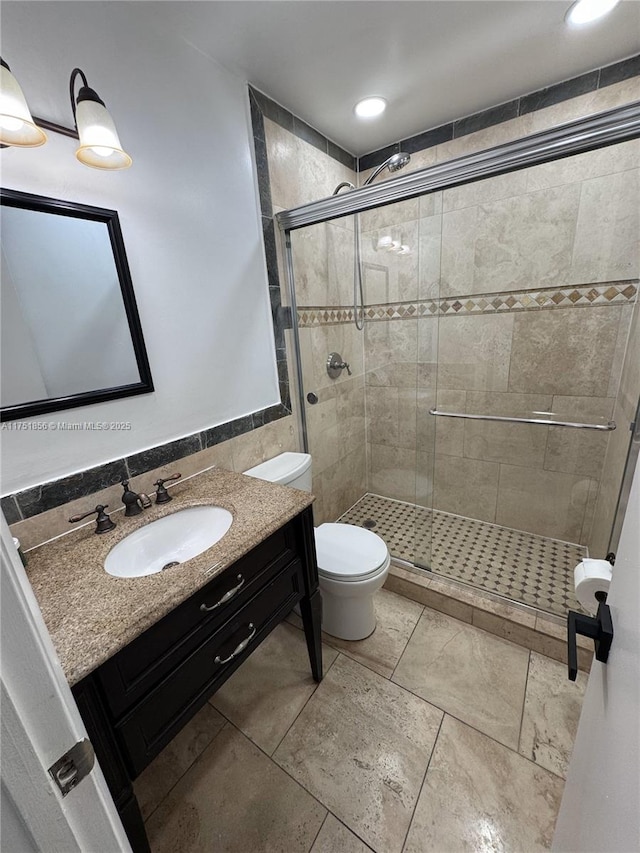 bathroom featuring a stall shower, vanity, toilet, and tile walls