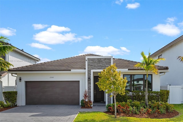 view of front facade featuring a garage, a tiled roof, decorative driveway, and fence