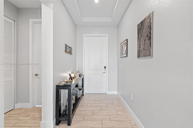 hall with wood tiled floor, baseboards, and a raised ceiling