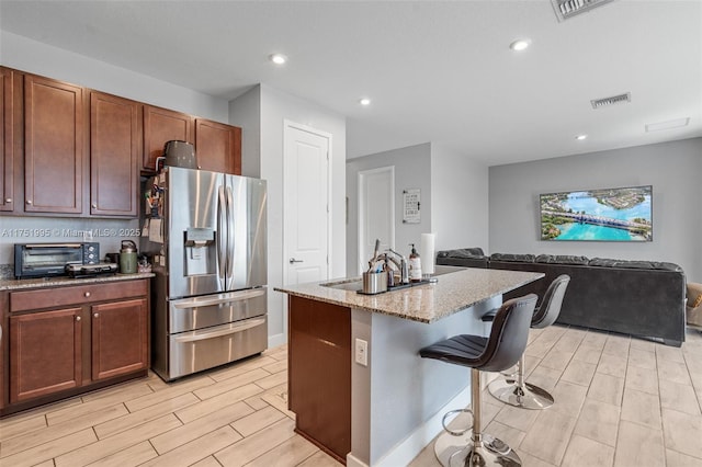 kitchen with stainless steel fridge, a toaster, open floor plan, wood tiled floor, and a kitchen bar