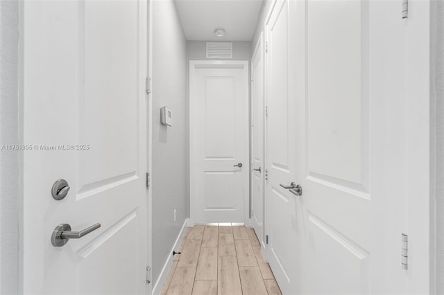 corridor featuring wood tiled floor, visible vents, and baseboards